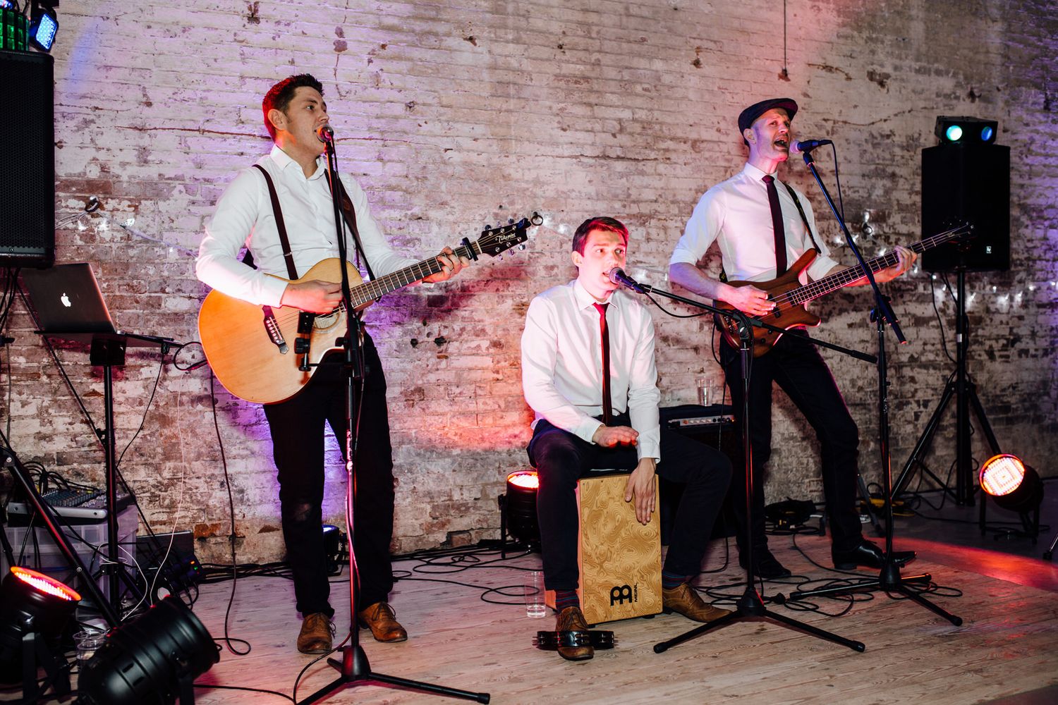 Wedding band performs on stage with guitars in a rustic brick venue with colored lighting.
