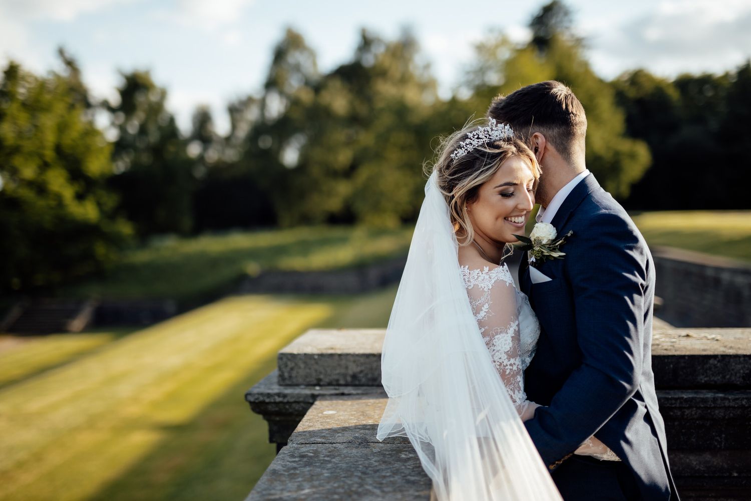Romantic wedding moment captured in golden sunlight on manicured garden grounds.