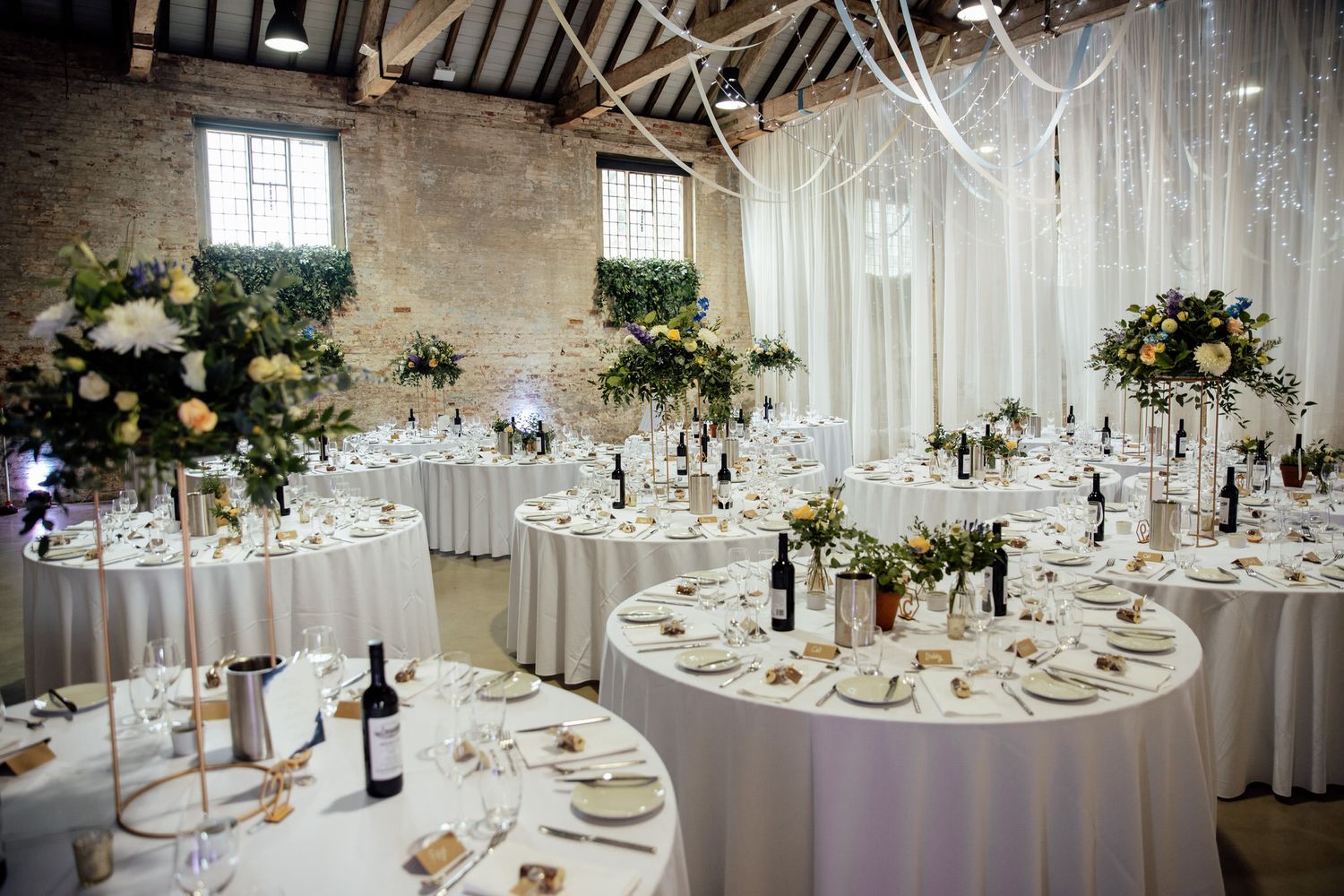 Beautifully decorated wedding reception tables with white linens and floral centerpieces in a rustic venue.