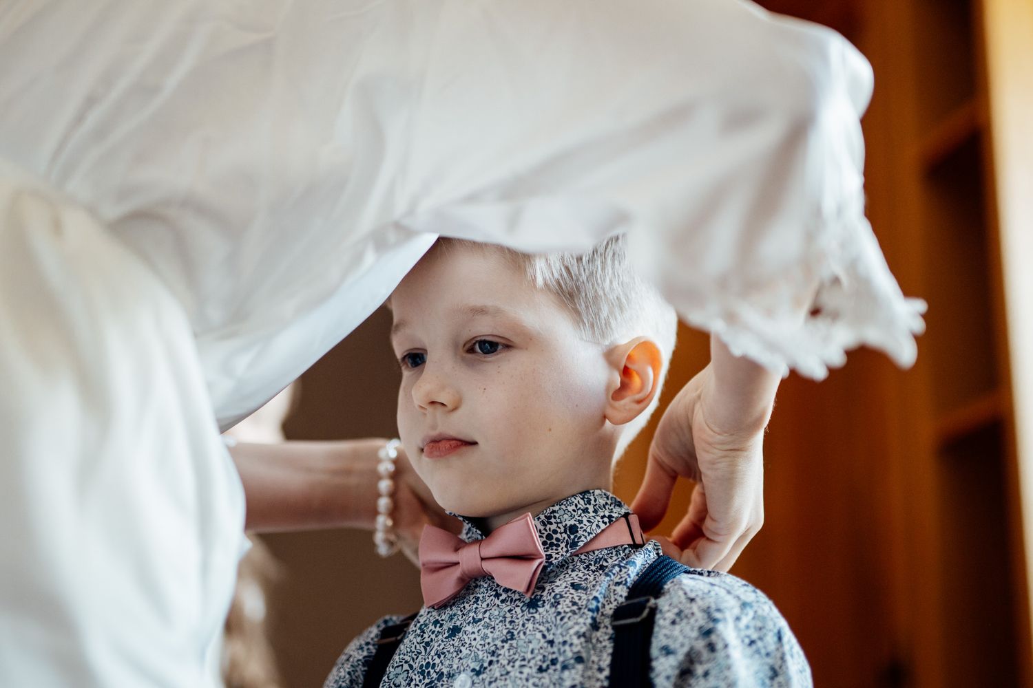 A child peeks through white fabric during a wedding preparation moment.