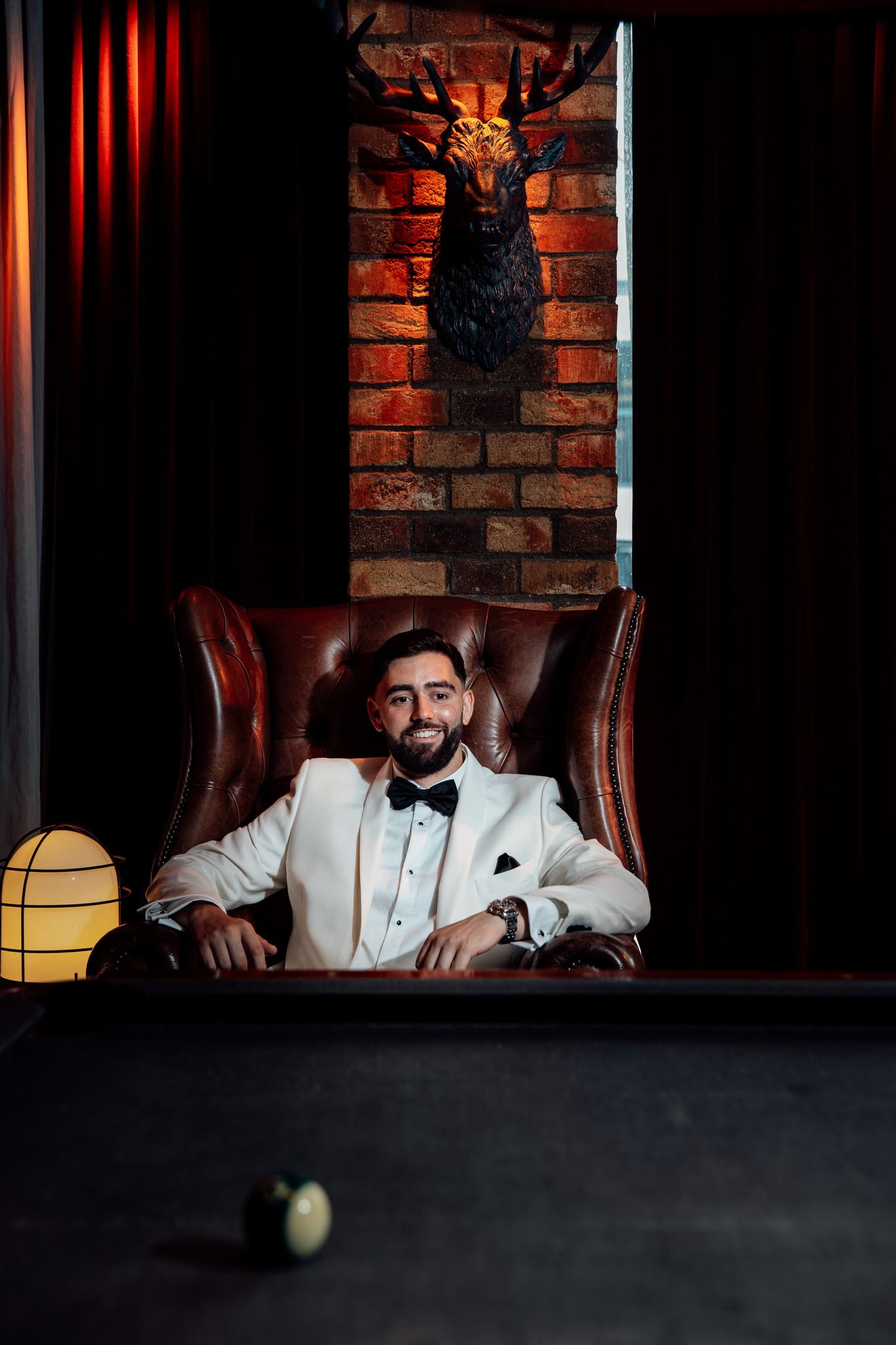 Moody portrait in white tuxedo against brick wall with dramatic lighting.