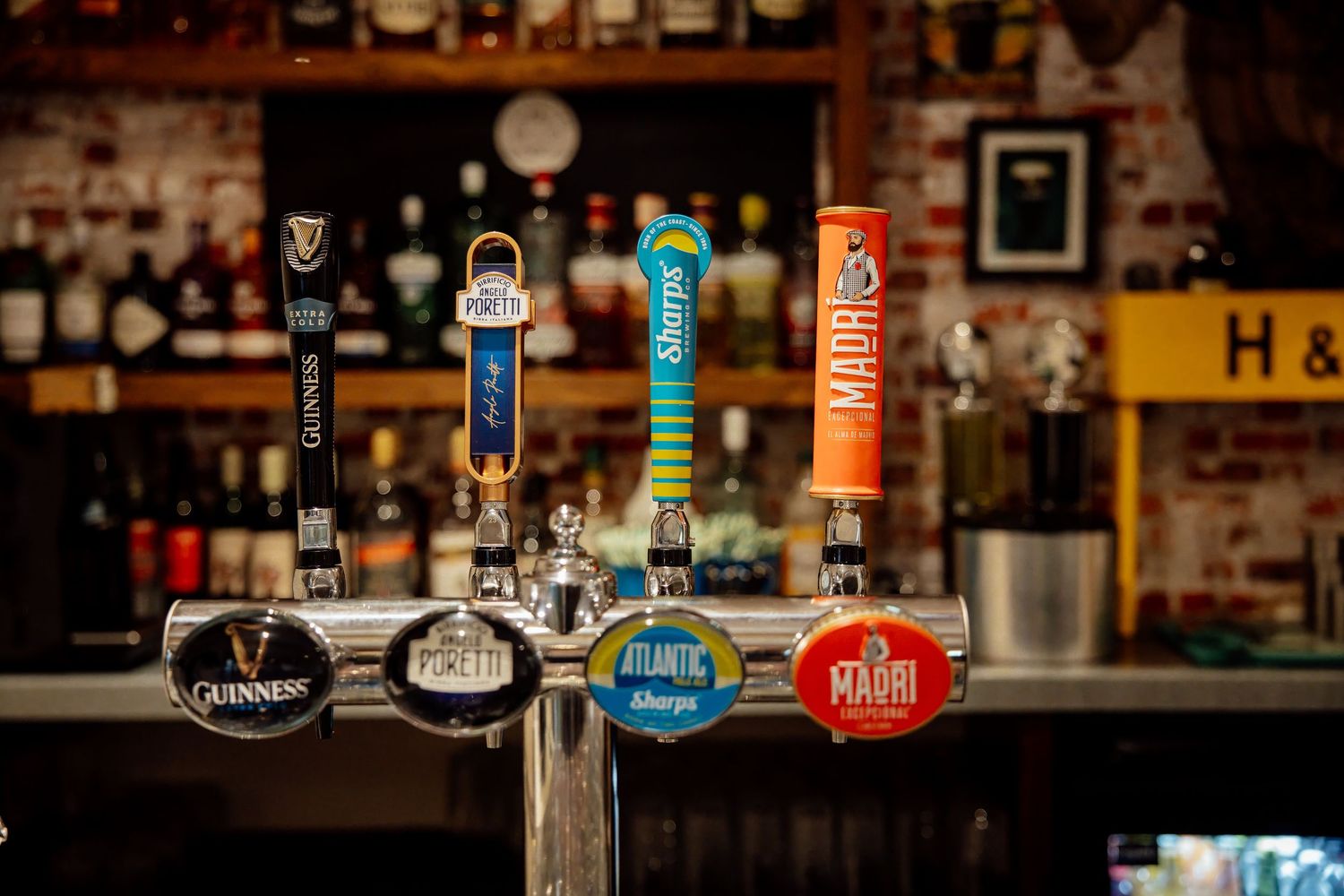 Multiple beer tap handles including Guinness, Atlantic, Sharps, and Madri on a bar counter.