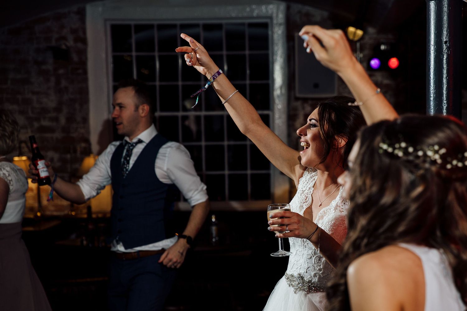 Wedding guests dancing and celebrating on a dark dance floor with festive lighting.