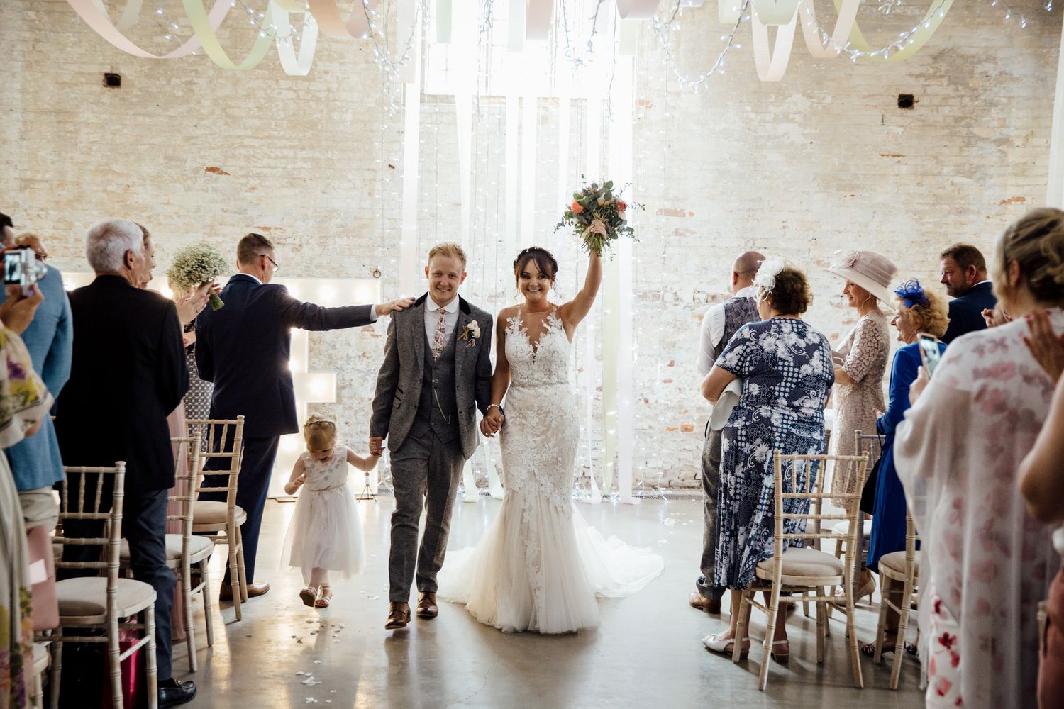 Panoramic view of wedding reception with guests celebrating in an elegant white venue.