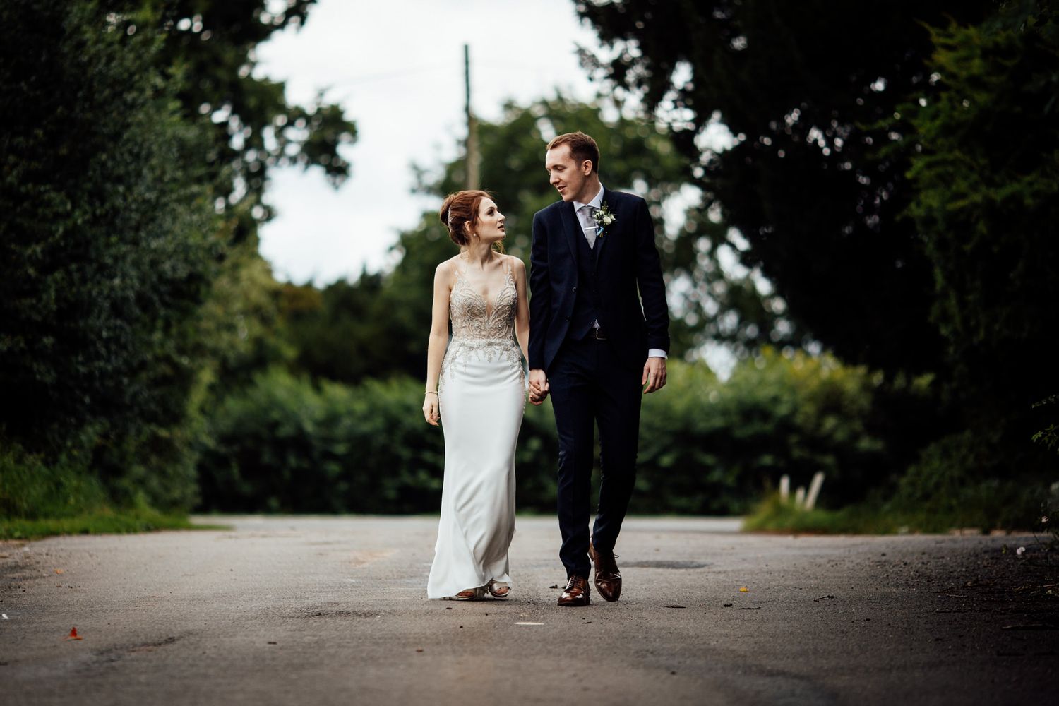 Couple walking along a tree-lined path during an outdoor wedding photo session.
