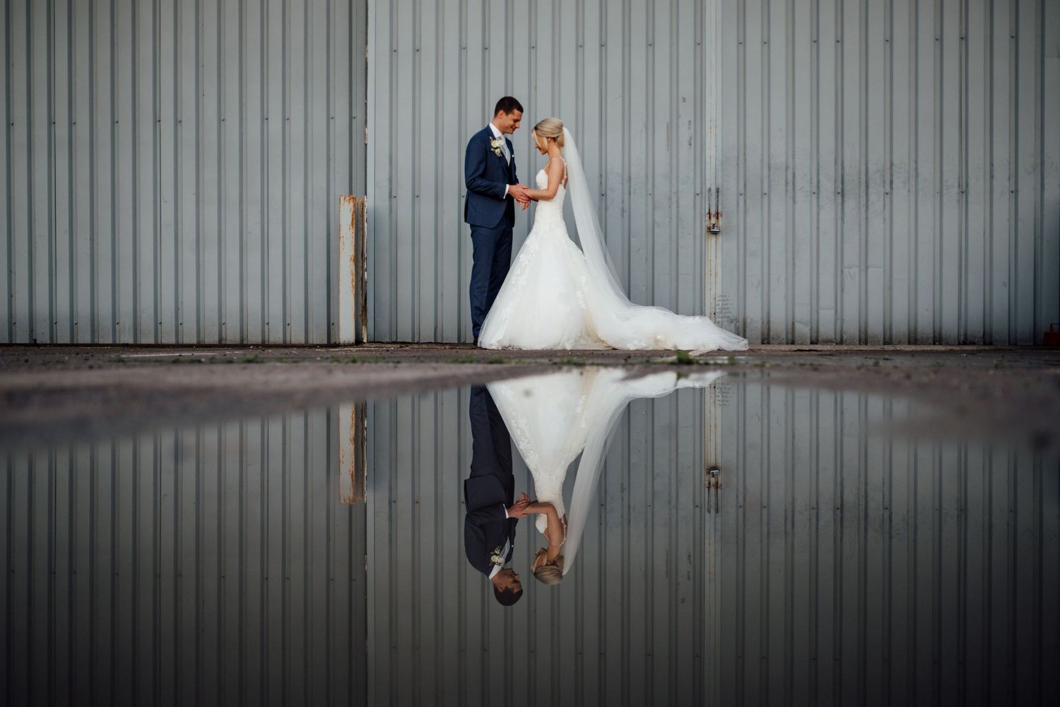 Wedding couple poses against industrial metal wall for artistic portraits.
