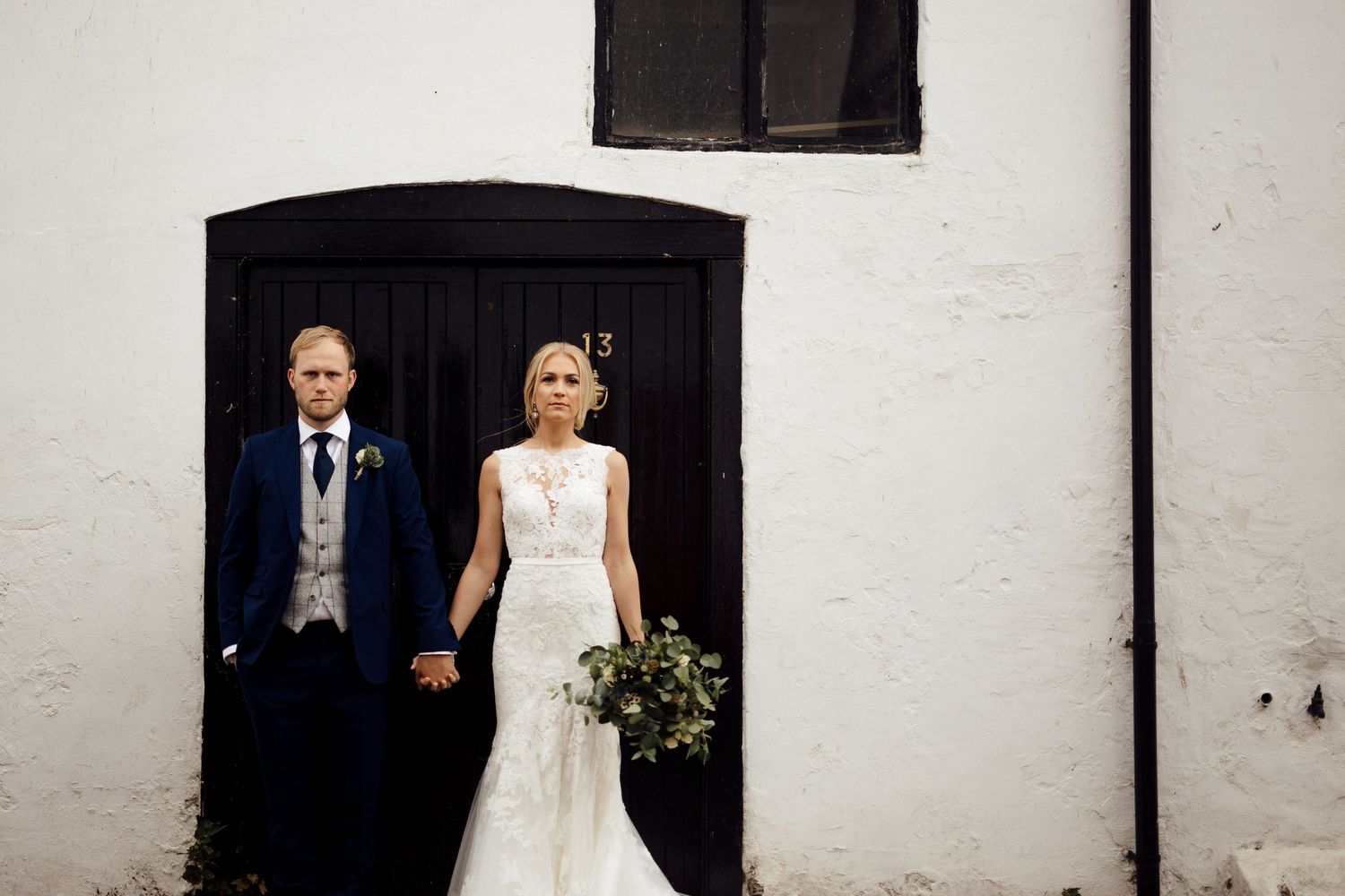 Wedding couple walking together against white industrial building wall.