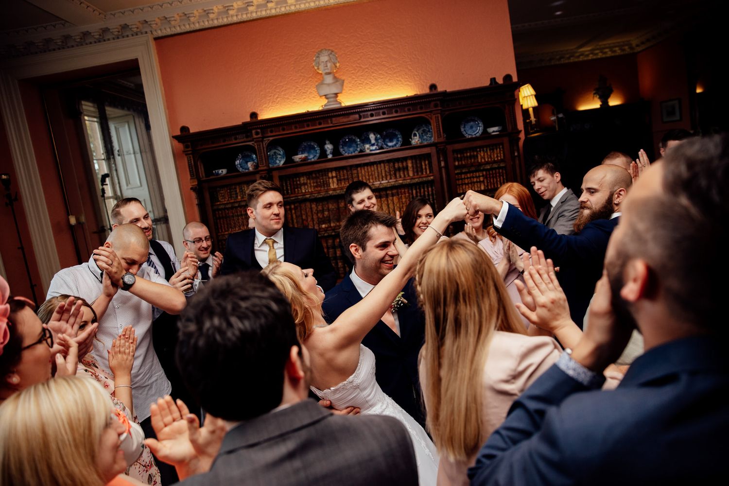 Wedding reception guests dancing and celebrating in a warmly lit indoor venue.