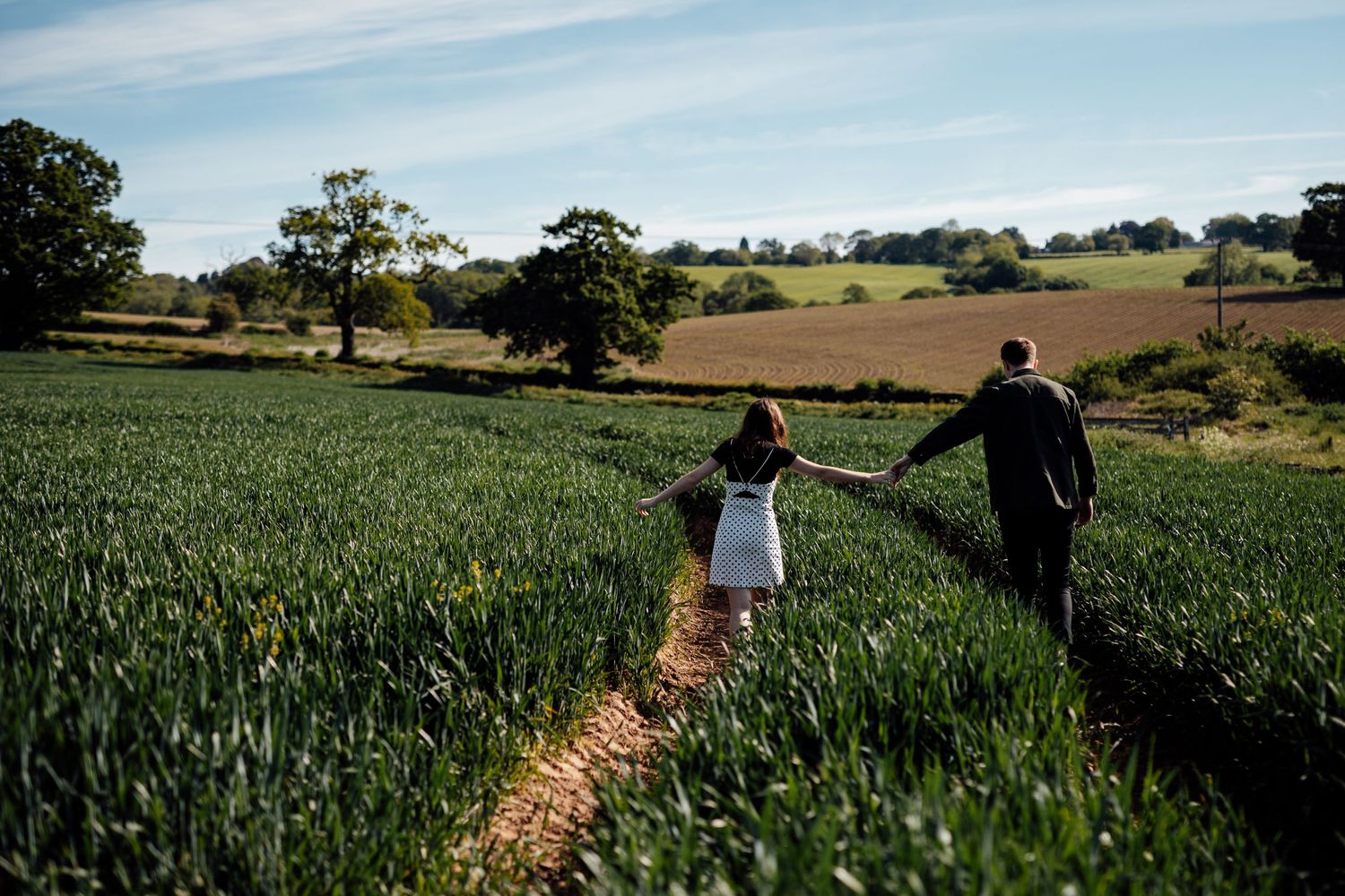 Panoramic view of a couple walking through rolling countryside fields under blue skies.