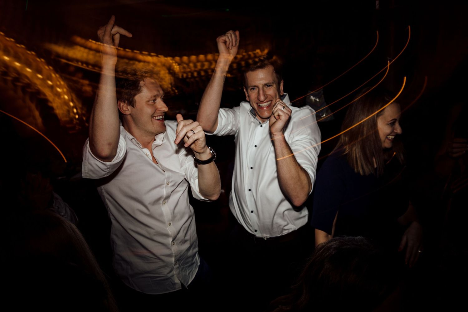 Wedding reception party with guests dancing and celebrating under warm lighting.