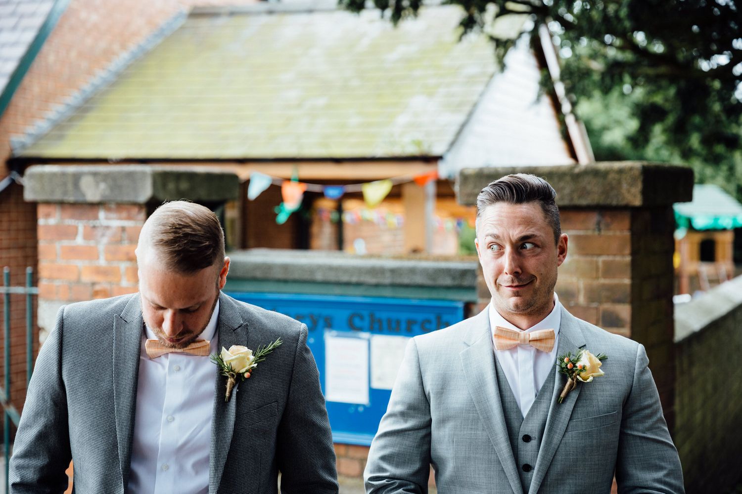 Wedding party members in grey suits and formal attire gather outside a brick building.