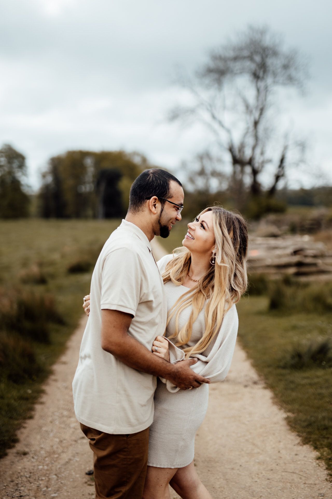 A romantic couple in light colored outfits share playful moments together on a dirt path in nature.