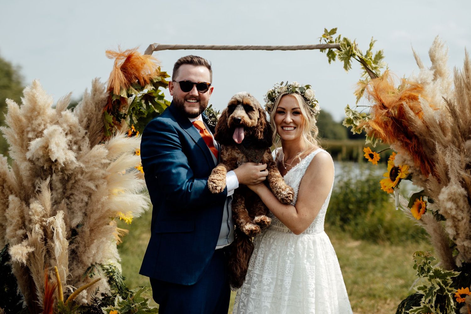 Wedding couple posing with their dog under a floral arch with pampas grass.