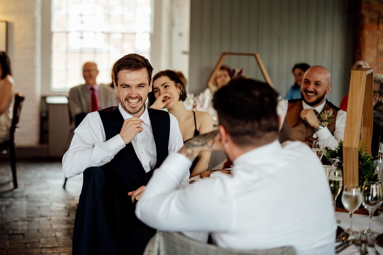 Wedding celebration candid moments with guests laughing and socializing at an indoor venue.