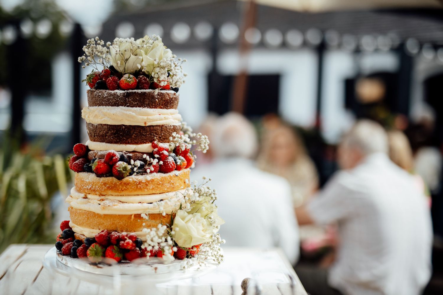 Naked wedding cake decorated with fresh berries and flowers on display.