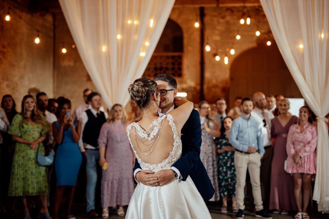 Wedding reception dance in rustic venue with string lights and white draping.
