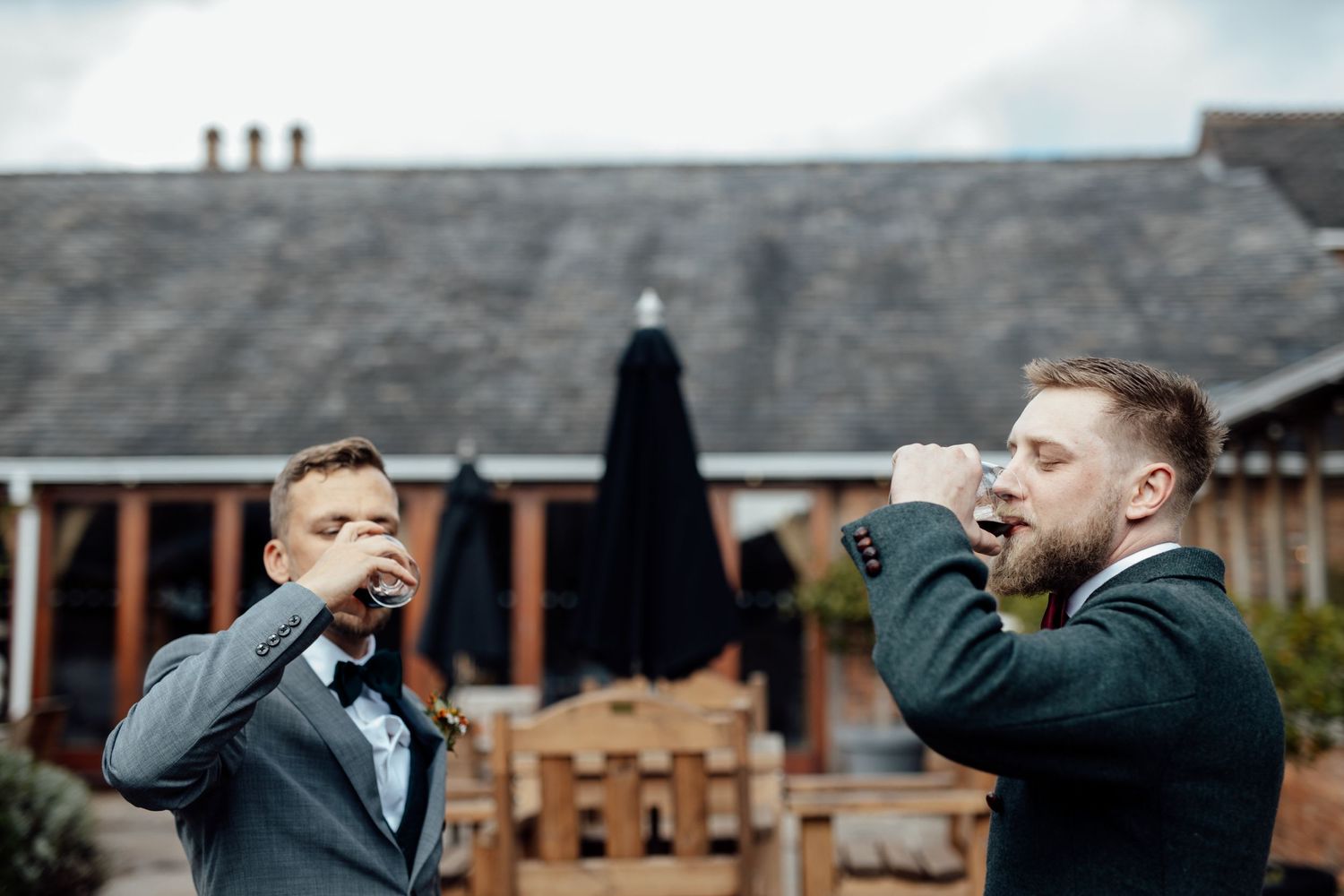 Groomsmen in formal attire sharing laughs and drinks during outdoor wedding celebrations.