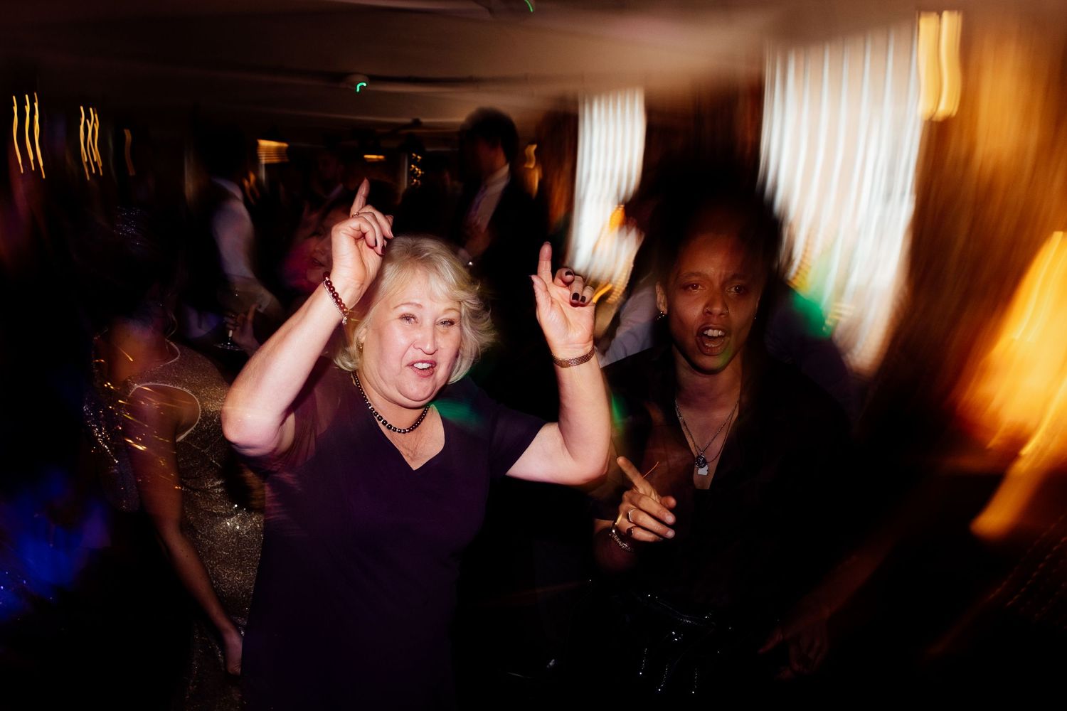 Wedding guests dance and celebrate on a dimly lit dance floor during a lively reception.