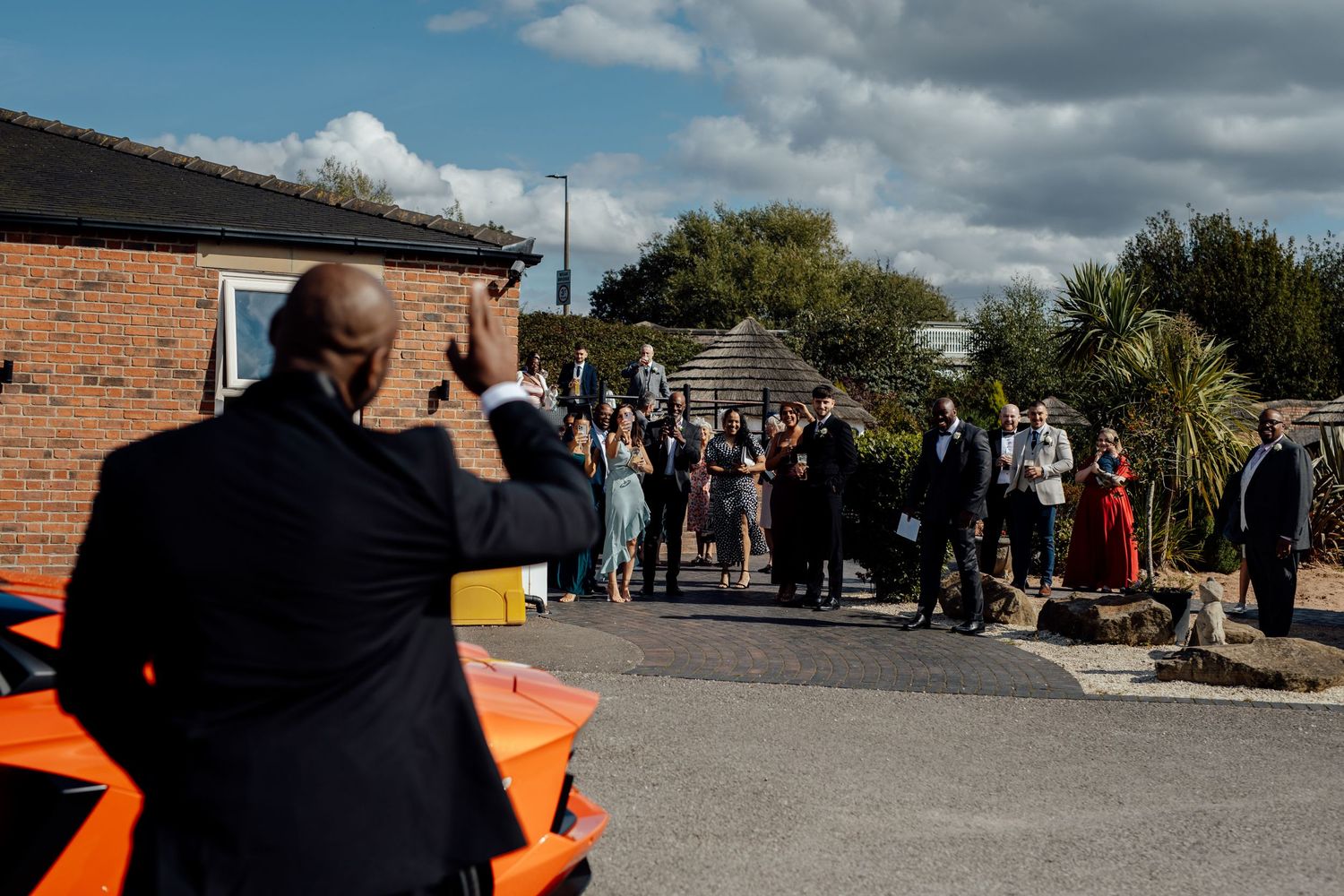 A photographer captures wedding guests gathered outside a brick building.