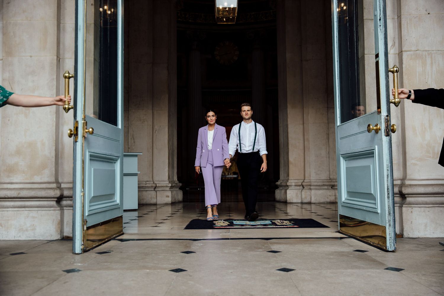 A romantic couple stands in front of elegant blue doors in a historic building hallway.