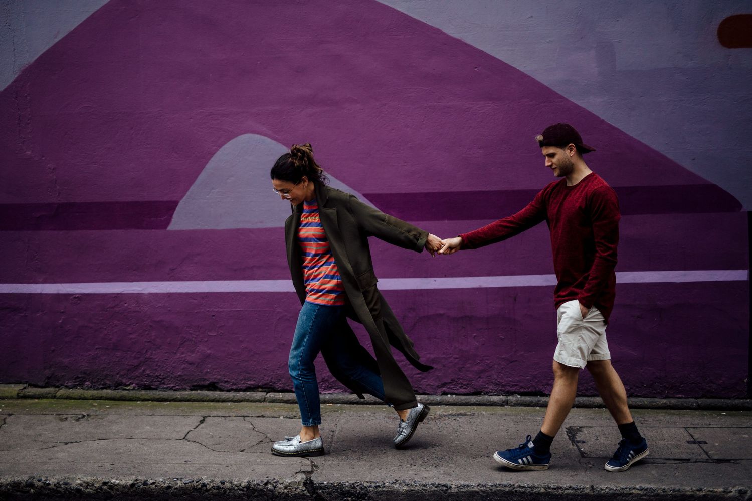 Playful couple poses against vibrant purple wall creating dynamic shadows and silhouettes.