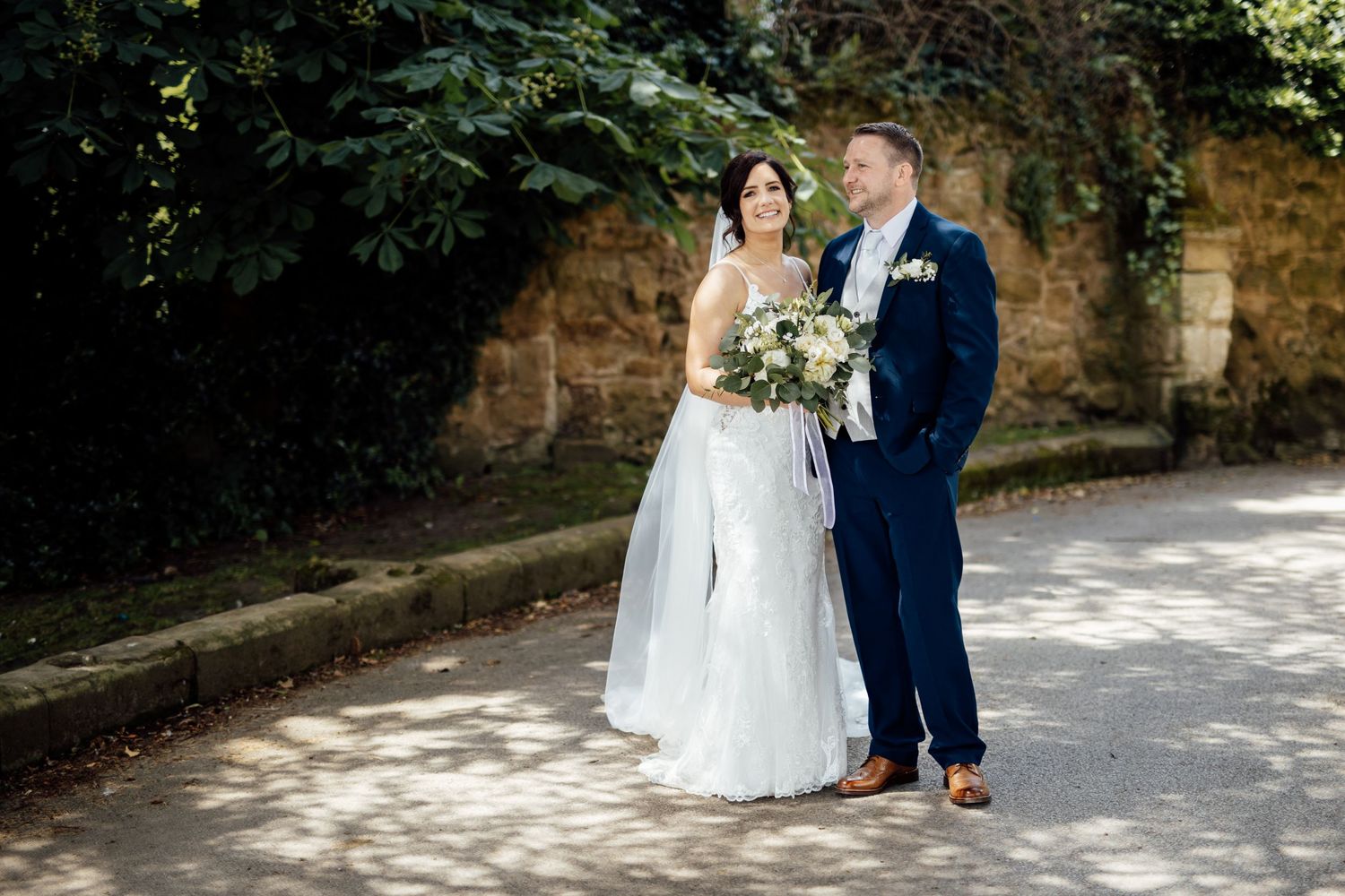 Wedding couple posing in a garden pathway with stone walls and greenery.