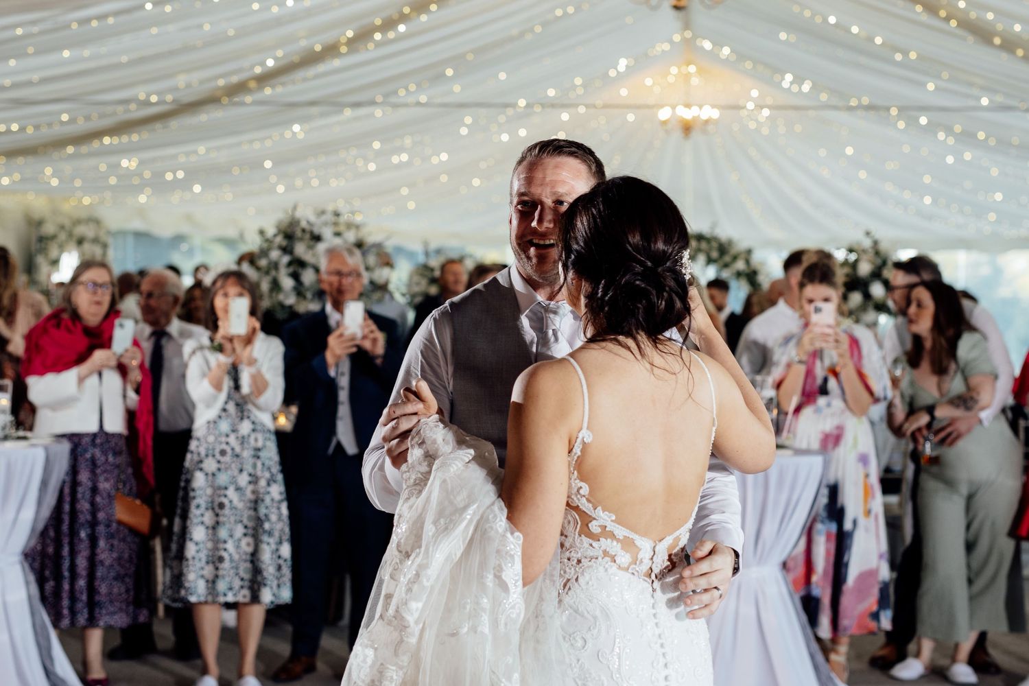 Romantic first dance moment under twinkling lights in an elegant wedding tent reception.