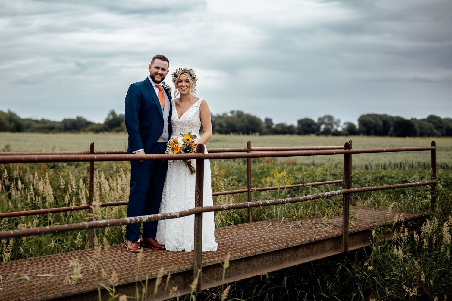 Couple walking along rustic wooden bridge in countryside wedding setting.