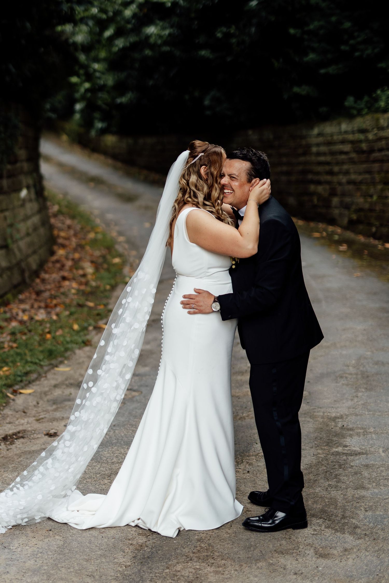 Couple sharing intimate moment on path with trailing wedding veil.