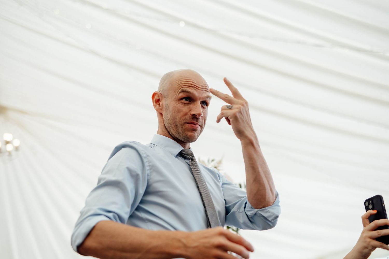 Wedding guests dancing and celebrating under a white tent canopy.