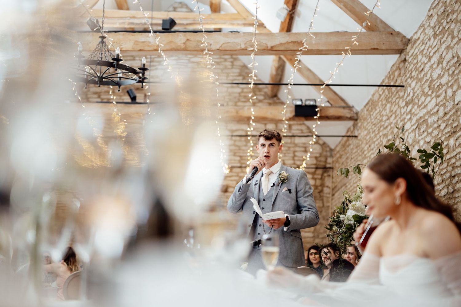 A wedding speech being delivered in a rustic barn venue with hanging lights.