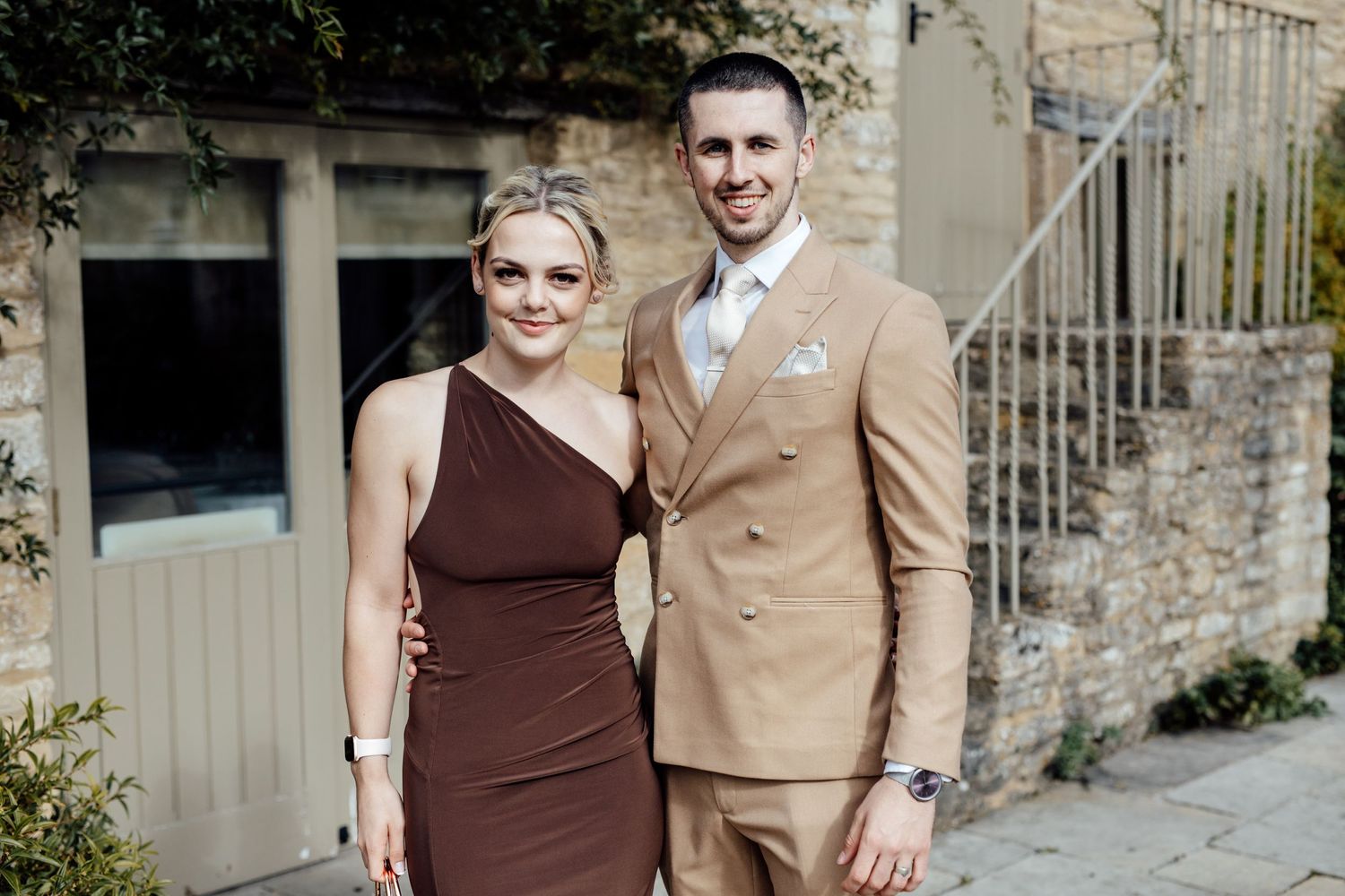 Wedding party members in burgundy and tan attire pose together outdoors.