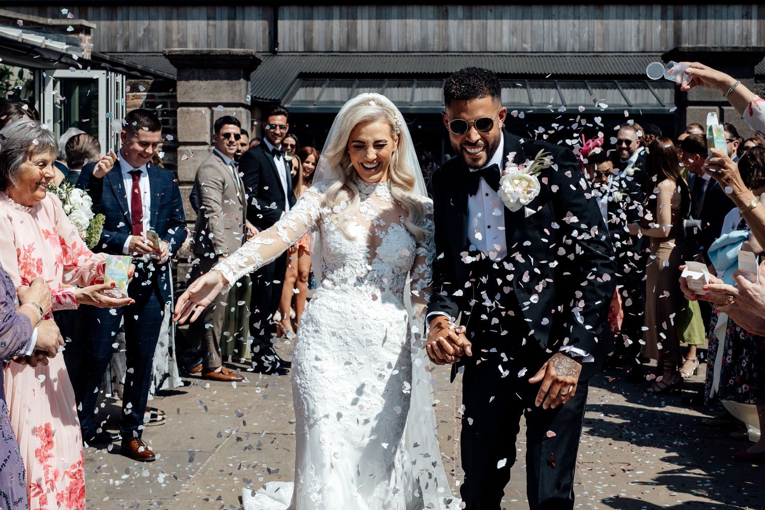 Wedding party and guests celebrate with confetti outside a venue.
