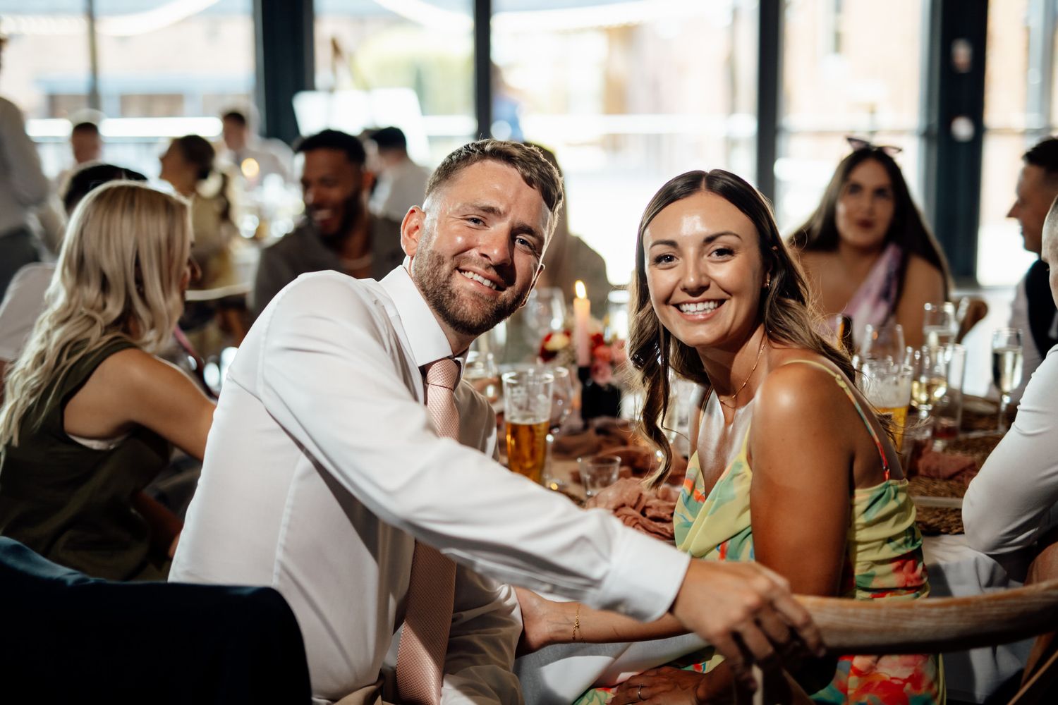 Wedding reception guests enjoying drinks and conversation at tables in rustic venue.