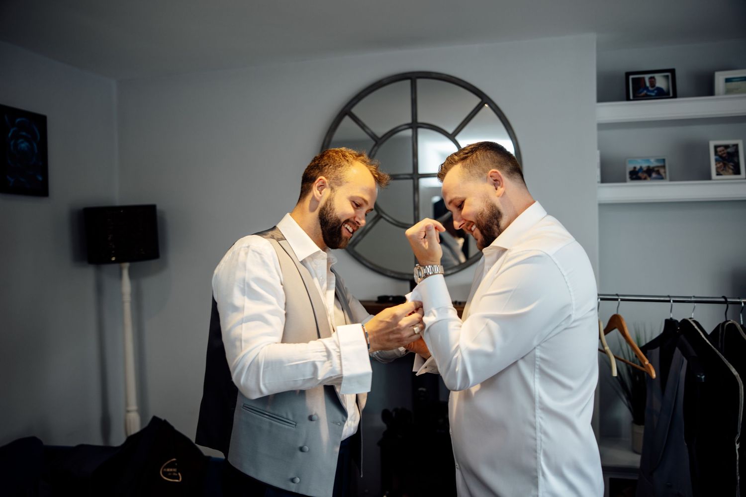 Two people in white shirts and vests sharing a joyful moment while getting ready.