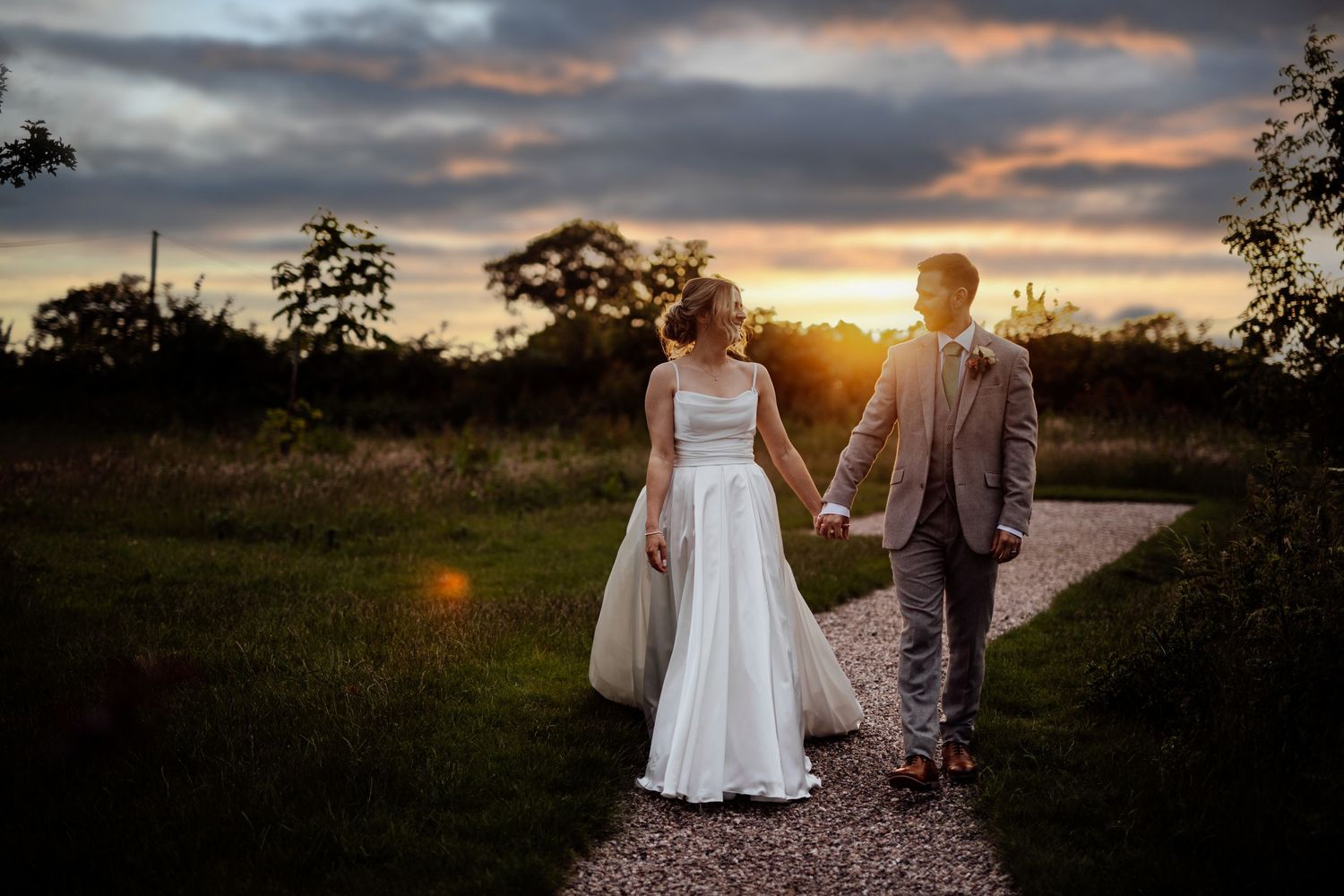 A couple walking along a countryside path during a dramatic sunset with cloudy skies.