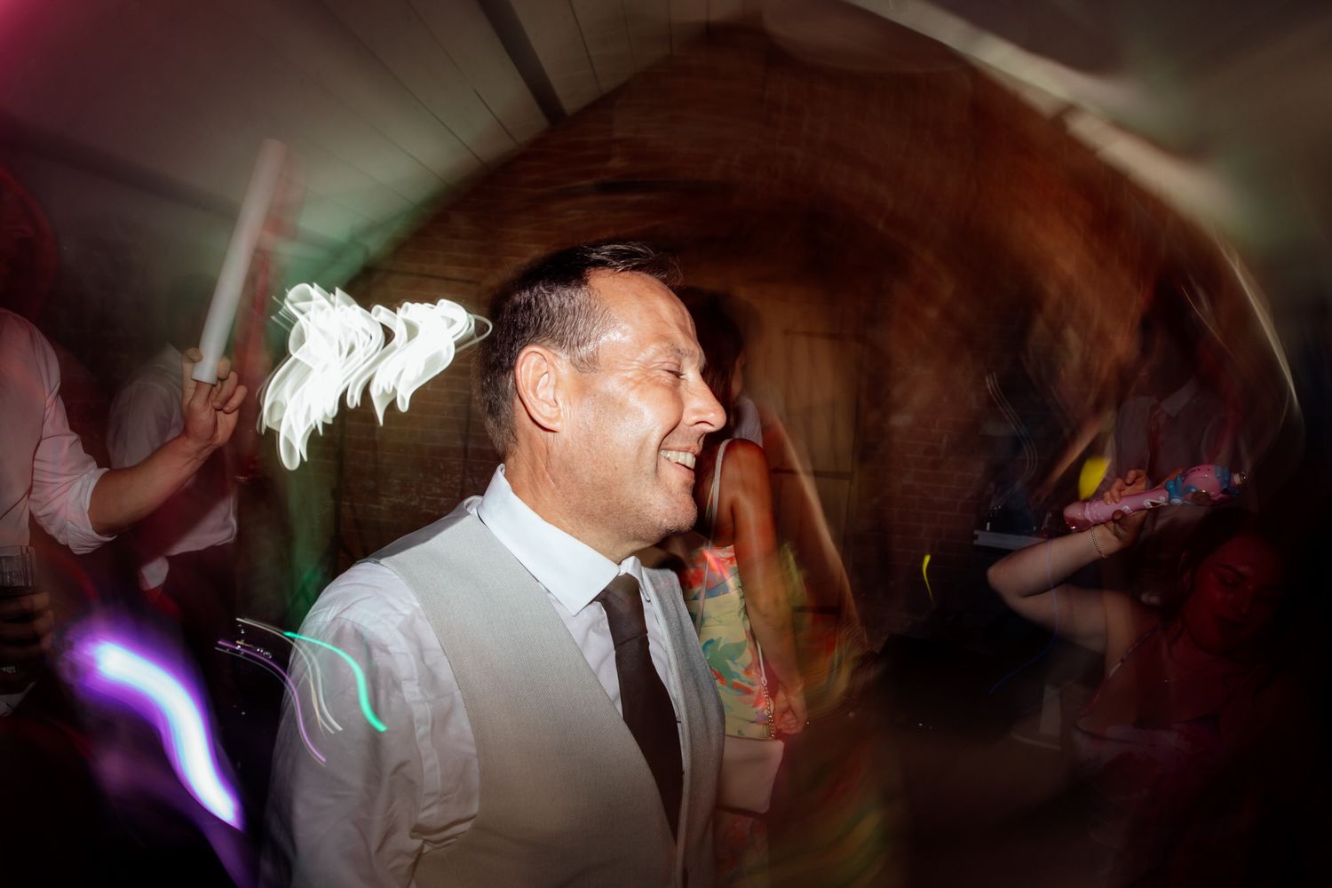 Dark reception venue with colorful party lighting and dancing silhouettes.