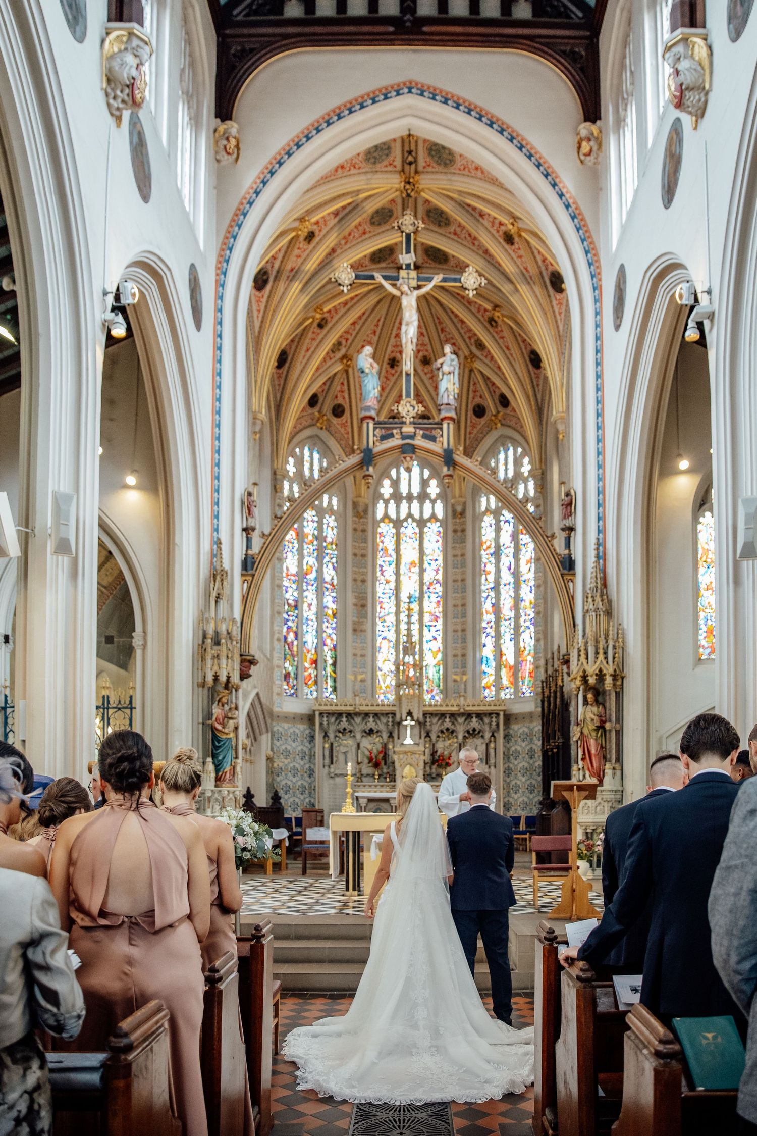 Wedding ceremony in ornate gothic church with vaulted ceilings and stained glass windows.