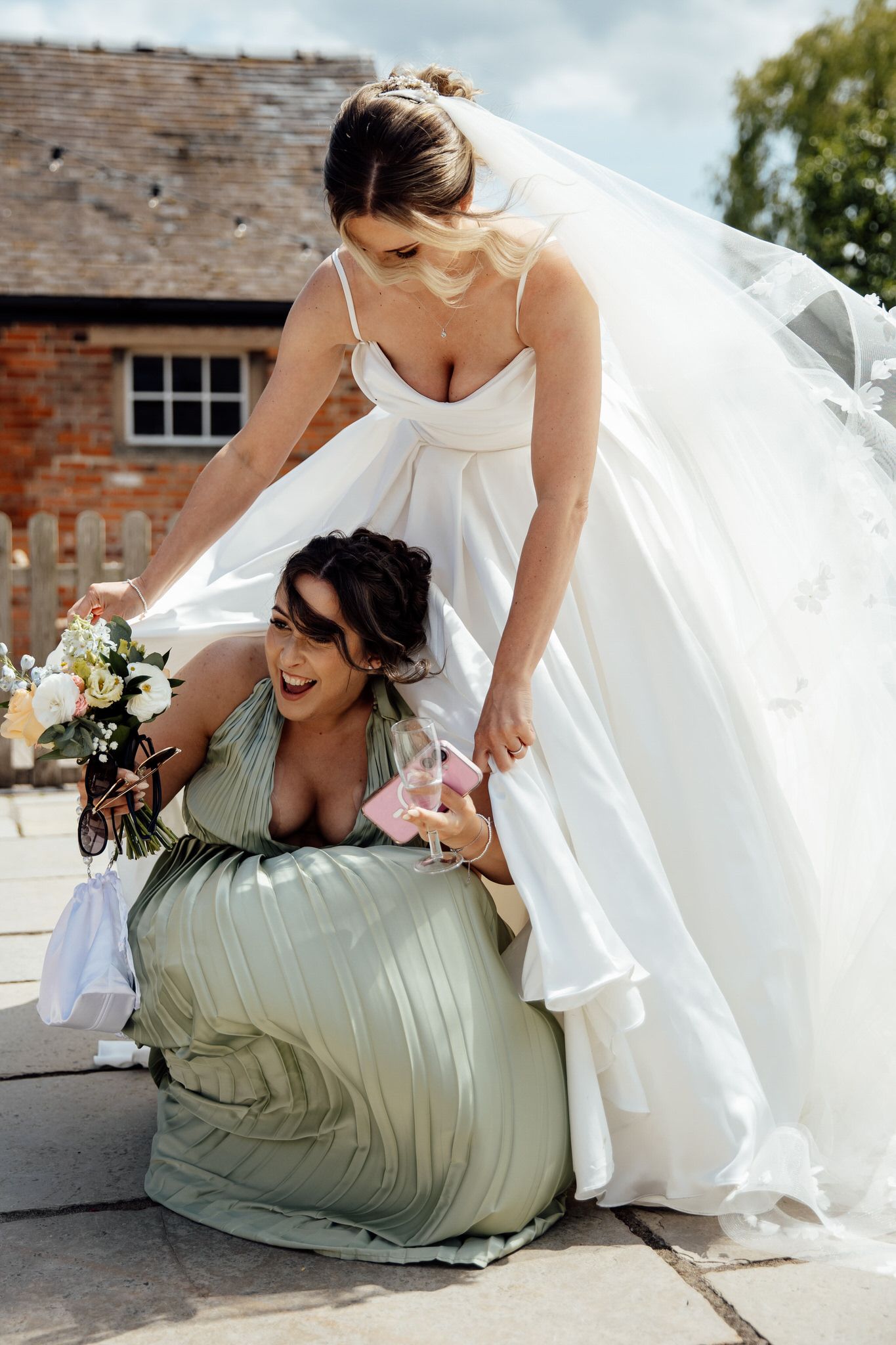 Wedding party members laughing and embracing on the ground in formal attire.