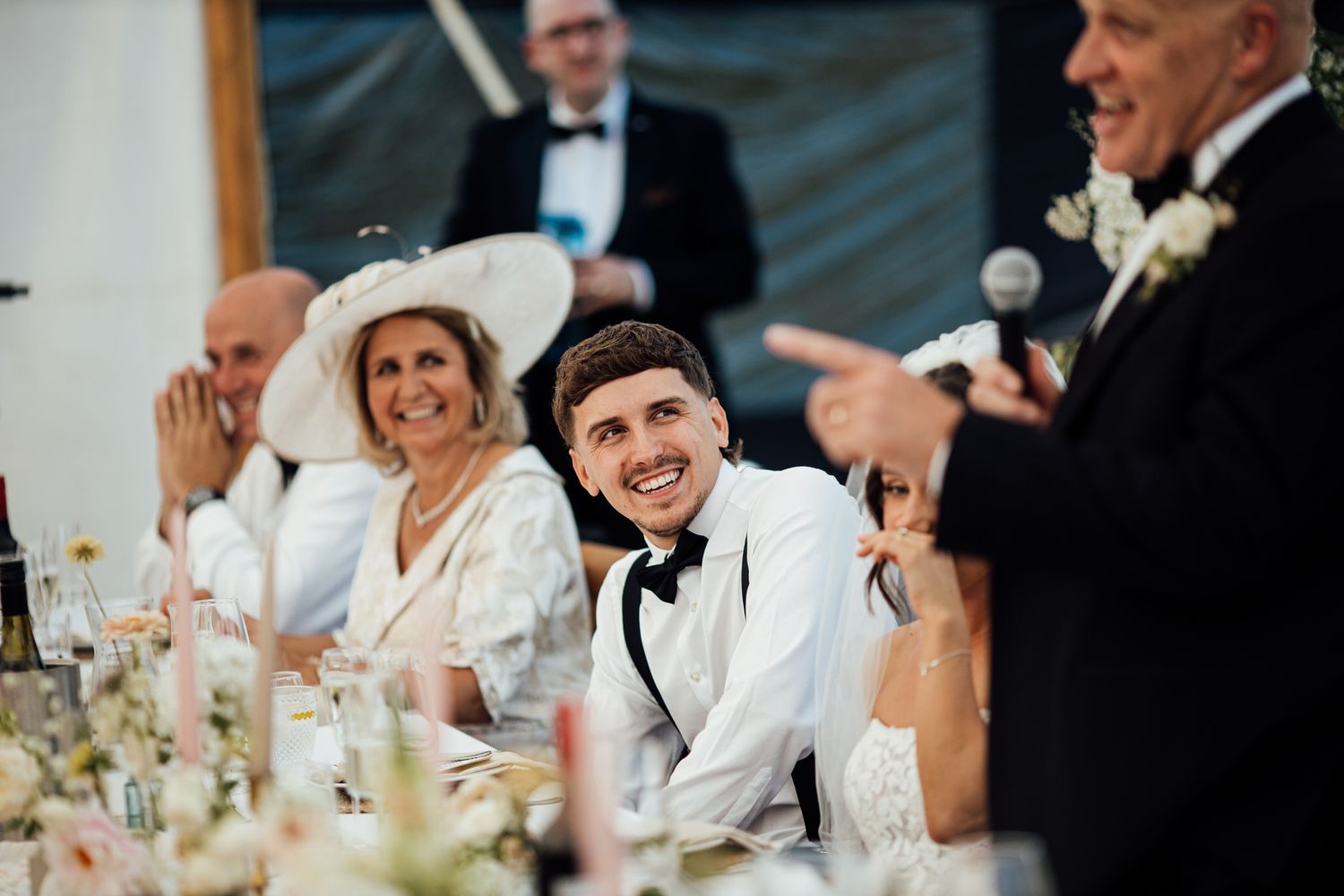 Wedding reception guests seated at elegant white-clothed tables with floral centerpieces.