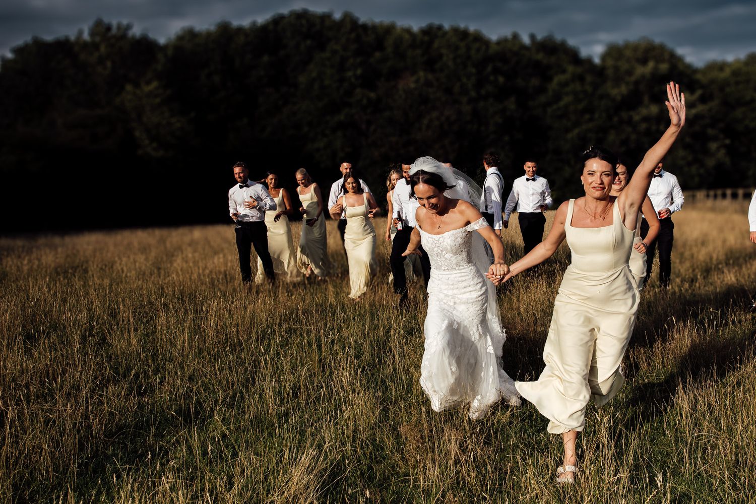 Wedding party running through golden field during sunset celebration.
