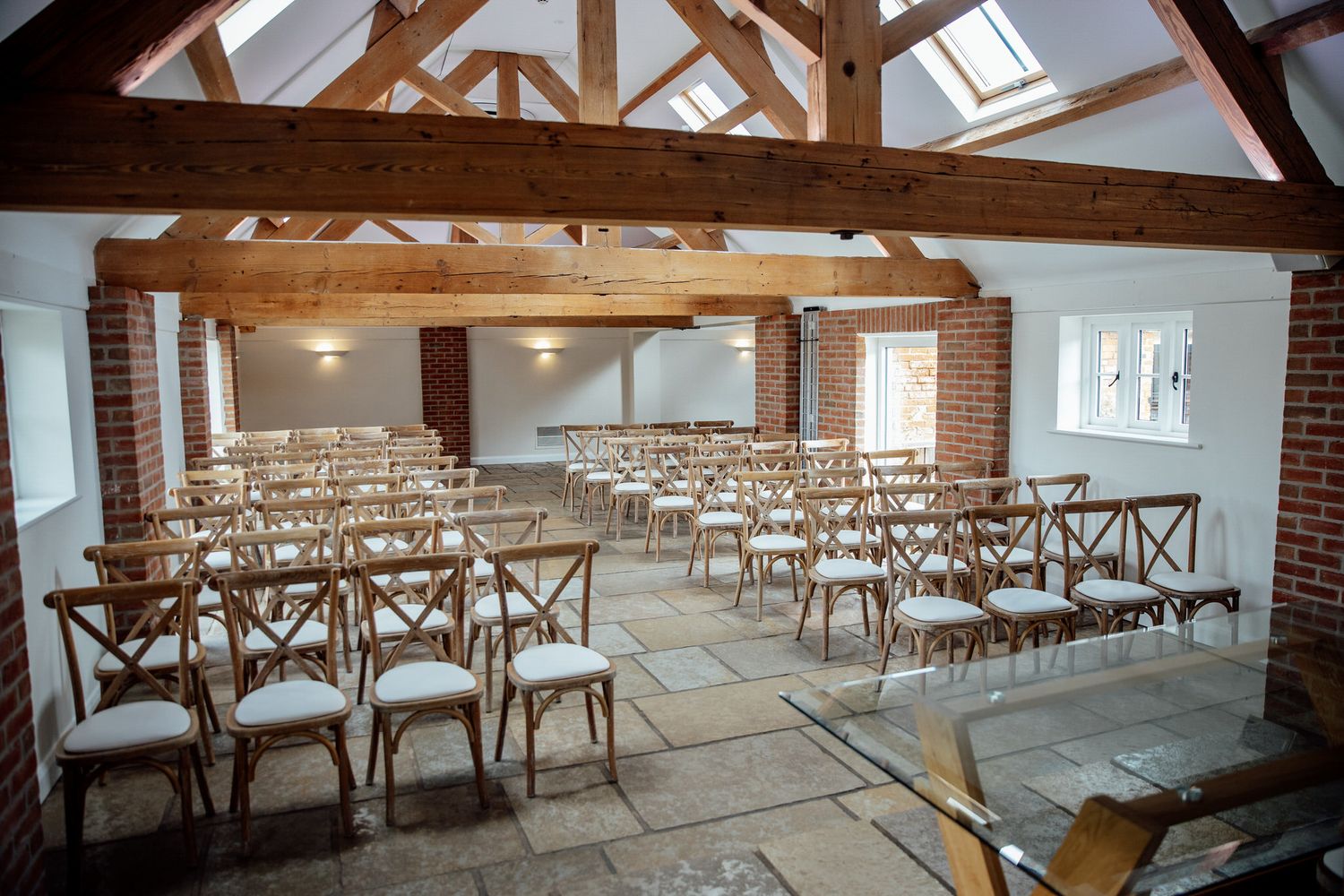 An empty wedding ceremony space with wooden cross-back chairs and exposed beam ceiling.