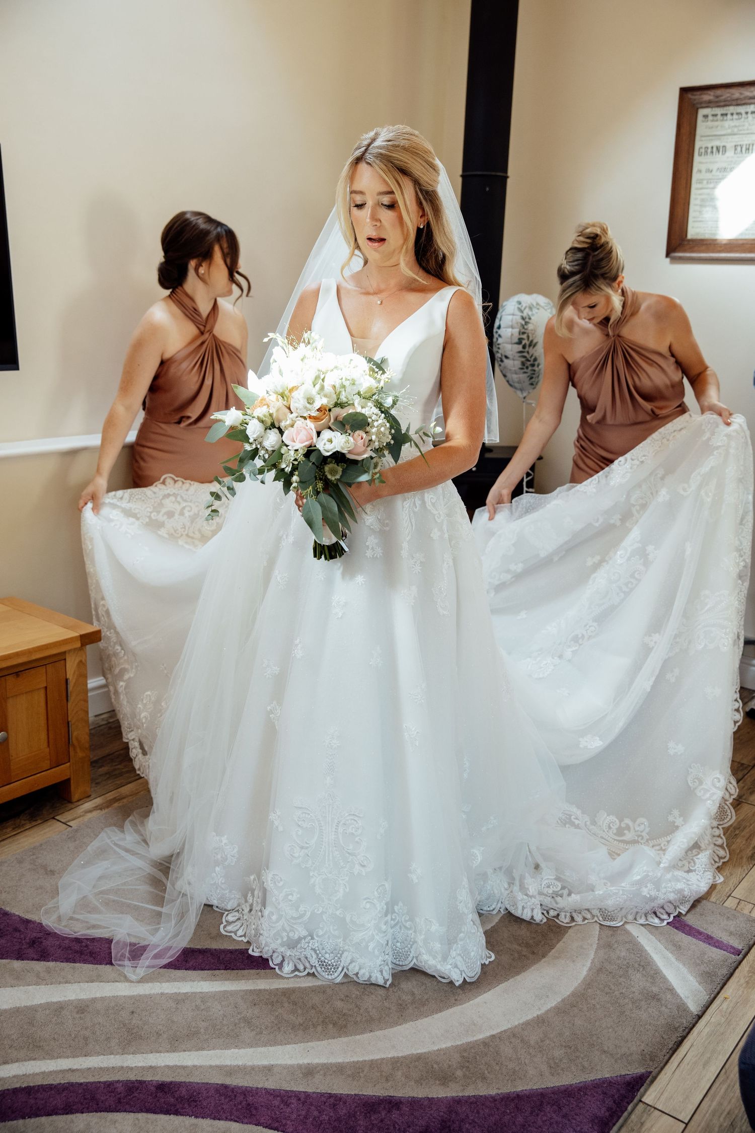 Bridesmaids help adjust the train of an elegant lace wedding gown.