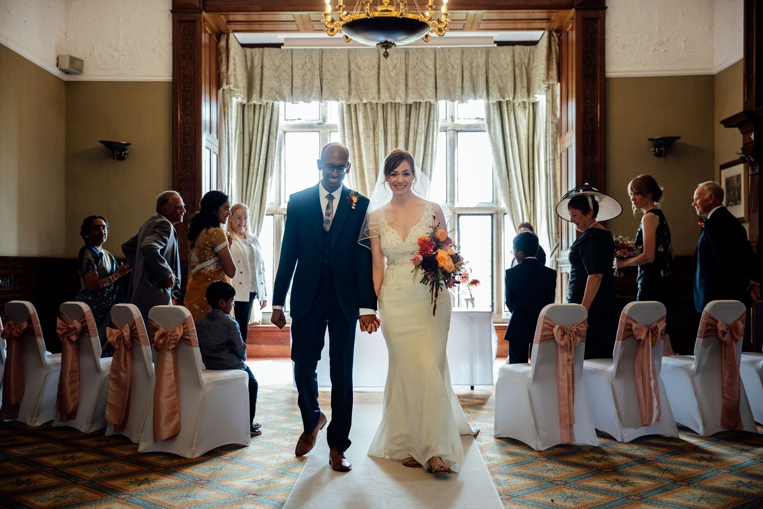 Wedding ceremony processional in elegant venue with pink chair decorations.
