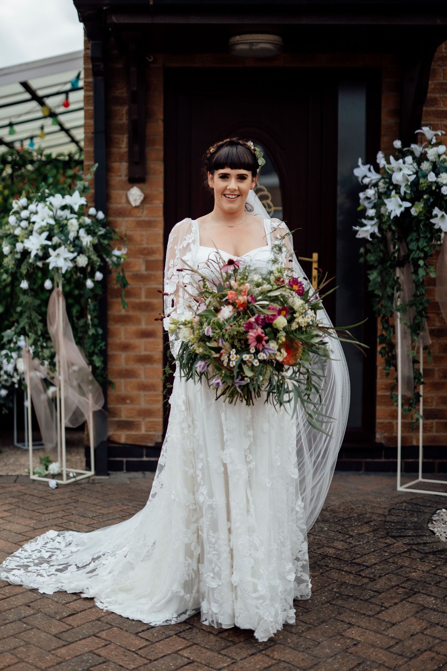 Beautiful lace wedding dress with floral bouquet displayed on brick patio.