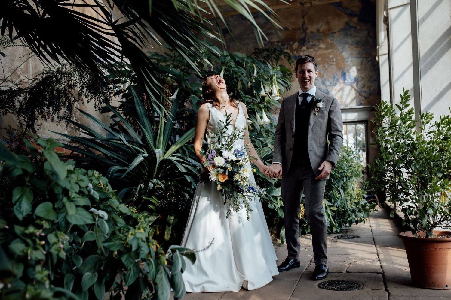 Wedding party walking through a lush greenhouse corridor with tropical plants.