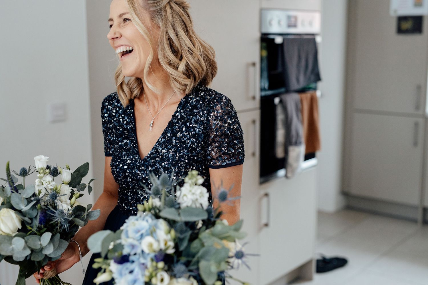 A person in navy polka dots arranges blue and white wedding flowers in a bright room.