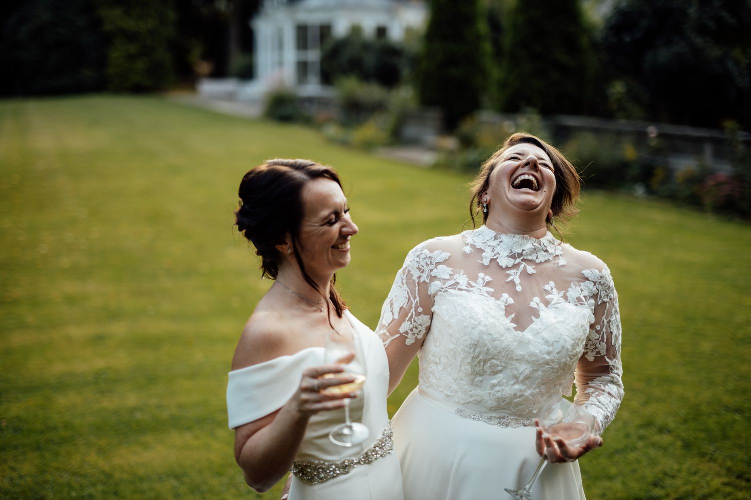 Wedding party laughing and celebrating together on a sunny green lawn.