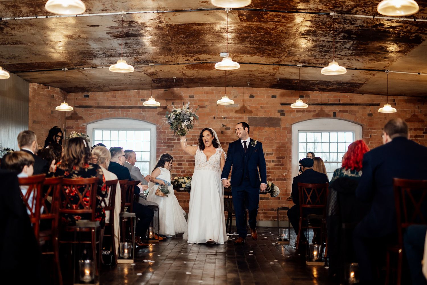 Reception venue with exposed brick walls and wooden beams lit by vintage pendant lights.