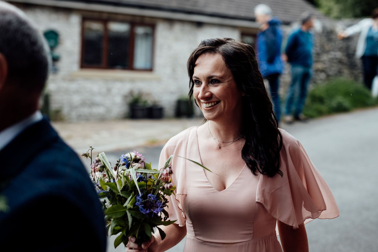 A bridesmaid in a blush pink dress holds a wildflower bouquet outdoors.